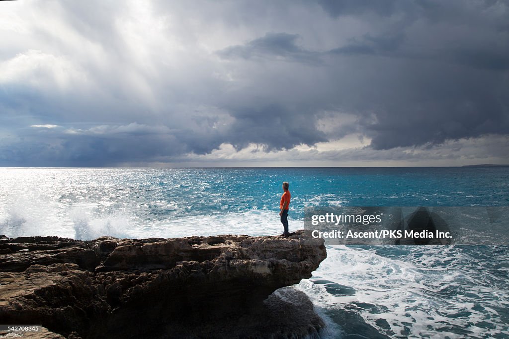 Distant man looks off to sea, from tidal rocks