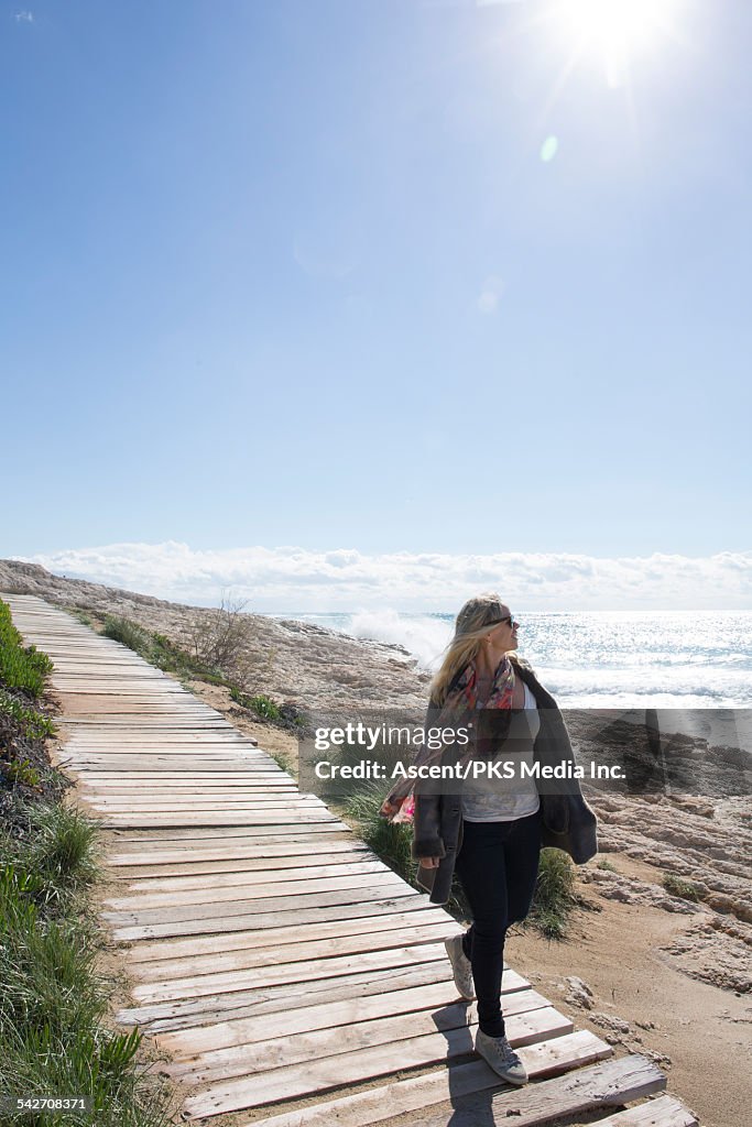 Woman walks along boardwalk, looks out to sea