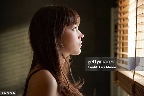 young woman looking out of window - patience foto e immagini stock