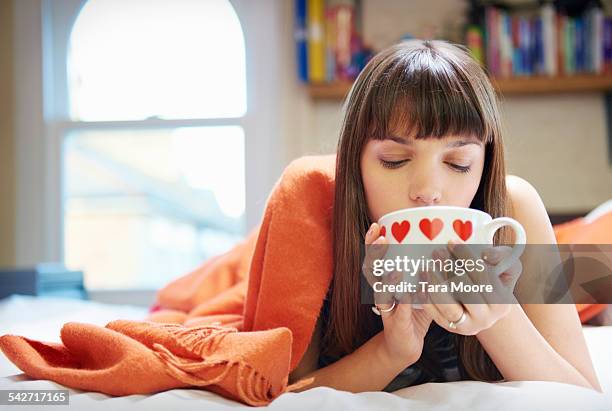 young woman in bed with blanket and tea mug - tea cup stock-fotos und bilder