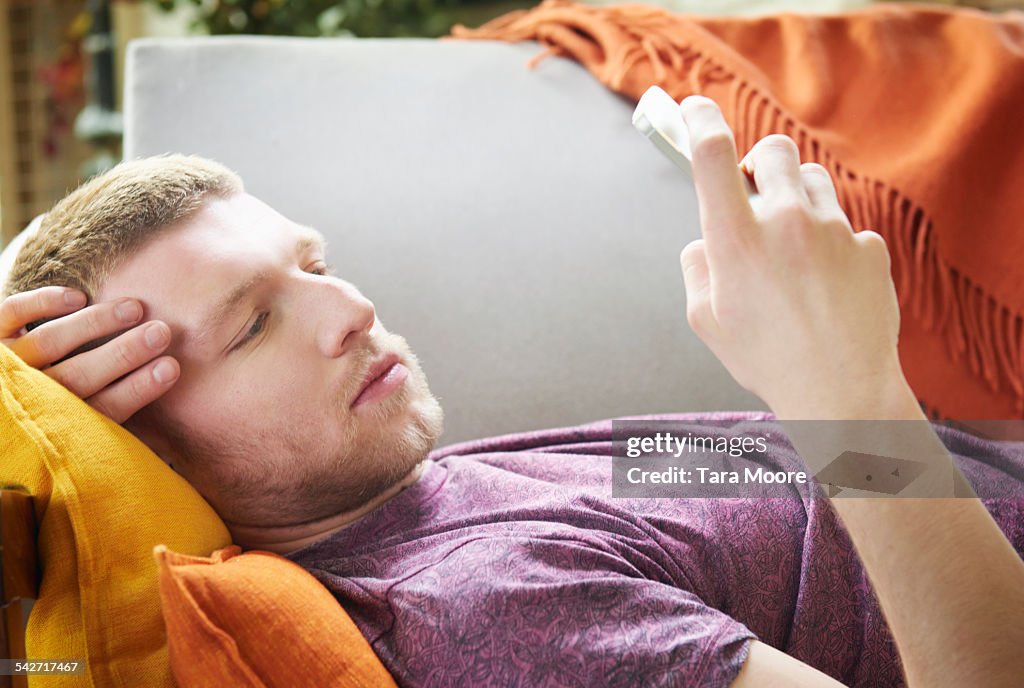 Young man with mobile lying on sofa