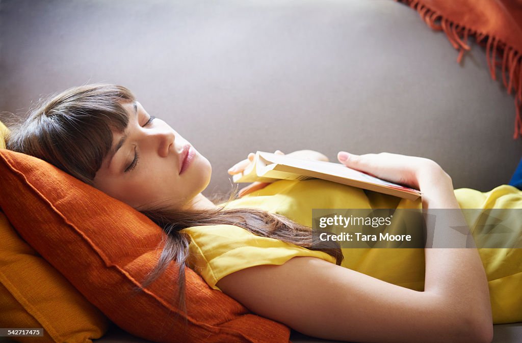 Young woman asleep with book on sofa