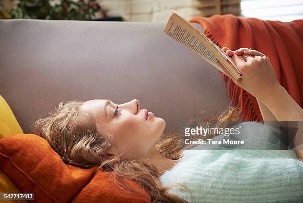 young woman lying on sofa reading - reading stockfoto's en -beelden