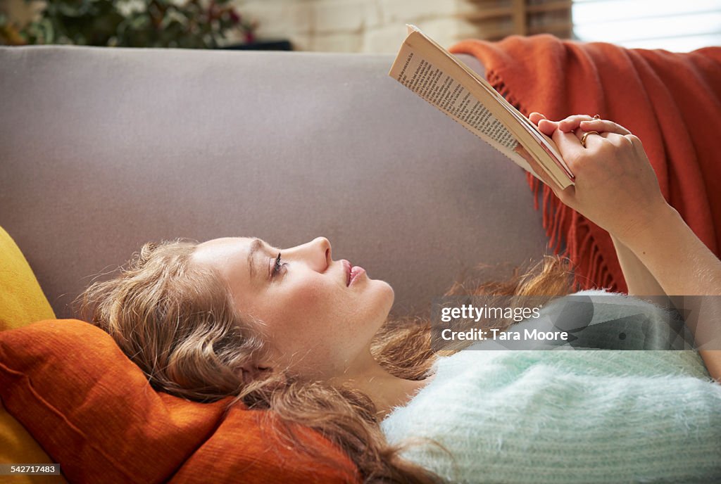 Young woman lying on sofa reading