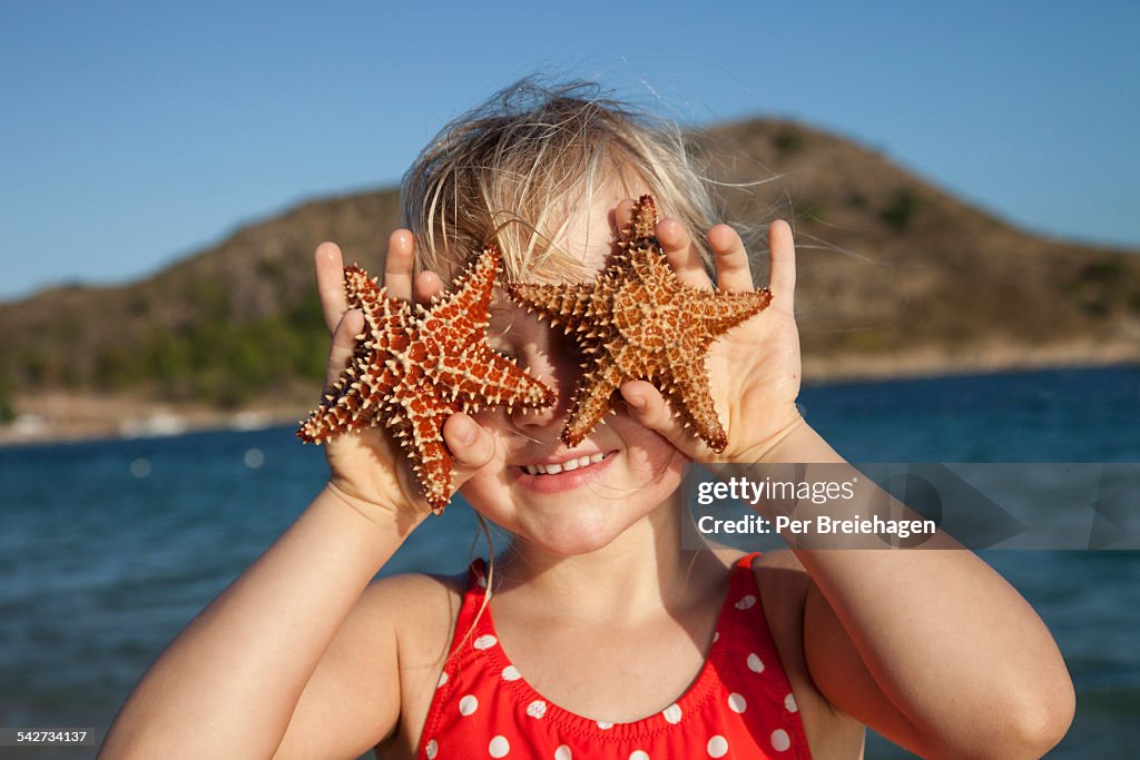 A young girl holding starfish over her eyes