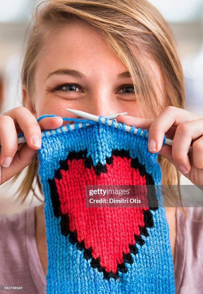 Young woman holding knitted red heart scarf