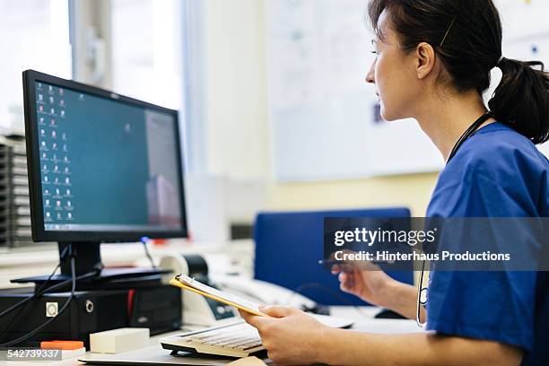 female mature doctor working on computer - medisch dossier stockfoto's en -beelden