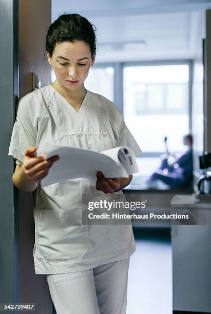 nurse with patient record leaning in door frame - blank frame stockfoto's en -beelden