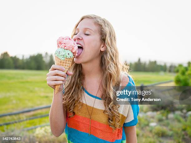 young woman licking ice cream cone outdoors - frau eistüte stock-fotos und bilder