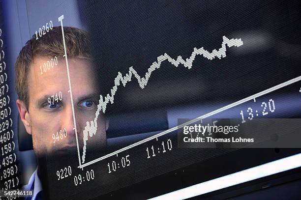 Trader sit at his desk under the day's performance board that shows a dive in the value of the DAX index of companies at the Frankfurt Stock exchange...