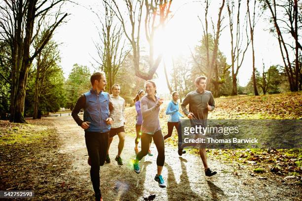 smiling friends running together in park - jogging stock-fotos und bilder