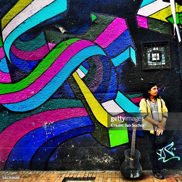 Colombian street musician stands in front of a graffiti artwork, created by an artist named Zas, in La Candelaria, Bogotá, Colombia, 18 February,...