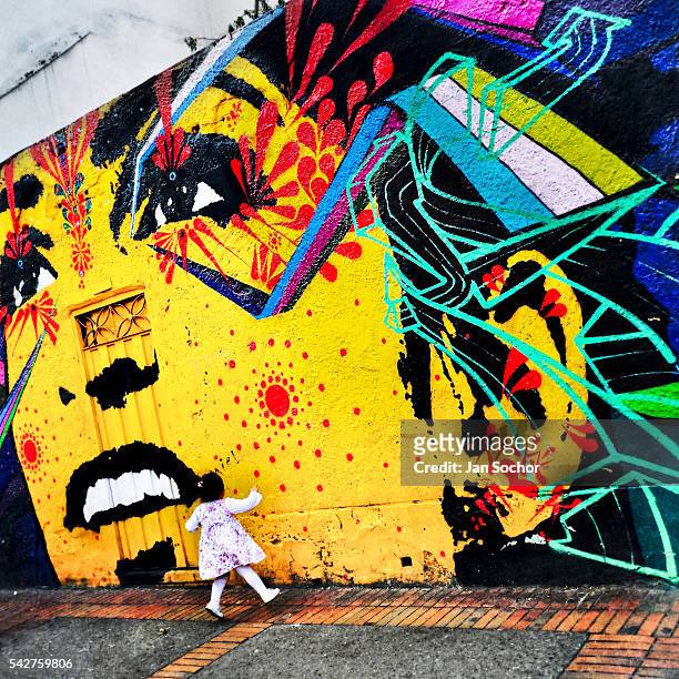 Colombian baby girl jumps in front of a graffiti artwork, created by artists named Stinkfish & Zas, in La Candelaria, Bogotá, Colombia, 18 February,...