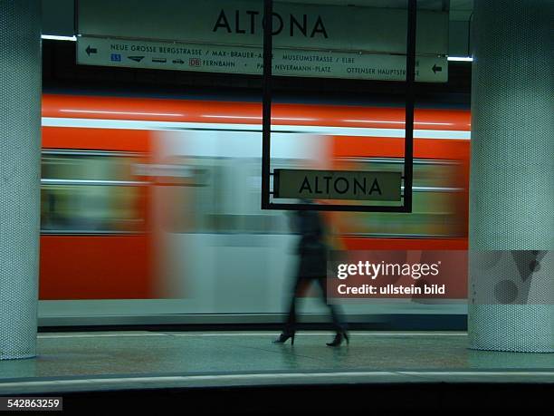Ein Frau steht am Bahnsteig des Bahnhofes Altona. Im Hintergrund ein einfahrender Zug der S-Bahn. Im Vordergrund ein Stationsschild mit der...