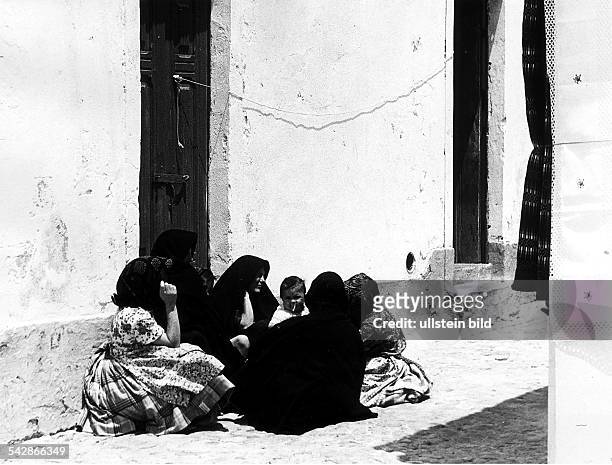 Frauen in schwarzen Gewändern sitzen mit ihren Kindern auf dem Boden einer Gasse in Nazare- 1969
