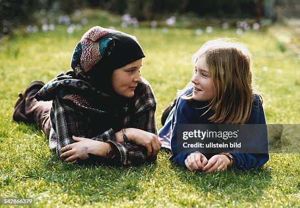 Ein türkisches und ein deutsches Mädchen liegen im Gras und unterhalten sich. Die kleine Türkin trägt ein Kopftuch. Symbolbild .