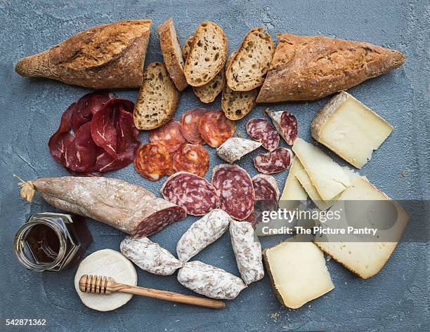 cheese and meat appetizer selection or wine snack set. variety of italian cheese, salami, bresaola, baguette, honey on over grey-blue concrete backdrop, top view. - bresaola stock pictures, royalty-free photos & images