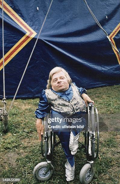 Peter Radtke*-Schauspieler, Schriftsteller, Dsitzt im Rollstuhl, in einem blauen Bühnenkostüm mit vor einem Zelt - undatiert