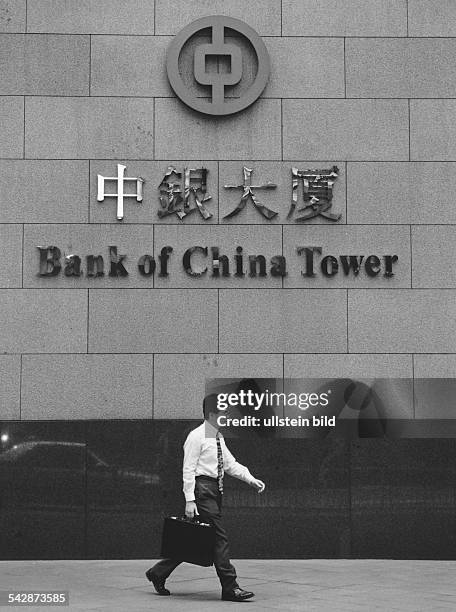 Ein Mann mit einem Aktenkoffer geht am Gebäude des "Bank of China Tower" vorbei. Die Fassade trägt den Namen der Bank in chinesischer und...