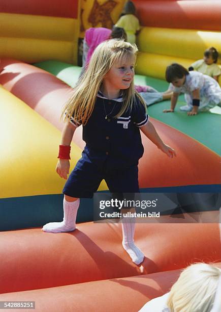 Ein kleines Mädchen mit langen blonden Haaren springt mit Socken auf einer aufblasbaren Kunststoffhüpfburg. Trampolin; Turnen; Spielen. Aufgenommen...