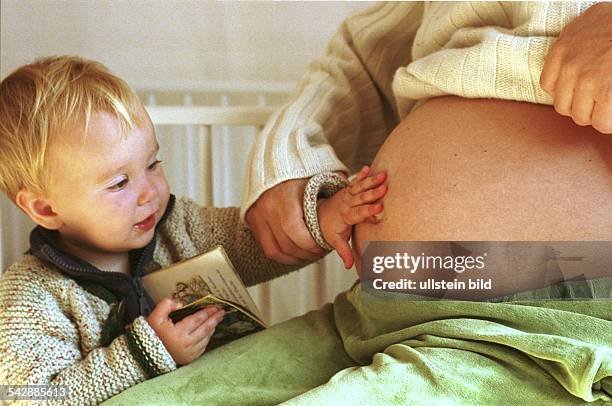 Ein kleiner Junge legt seine Hände auf den Bauch einer schwangeren Frau. .