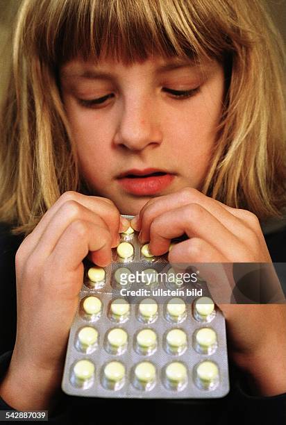 Ein junges Mädchen hält in Folie verschweißte Tabletten in den Händen. Medikamentenmissbrauch; Kind und Tabletten. .