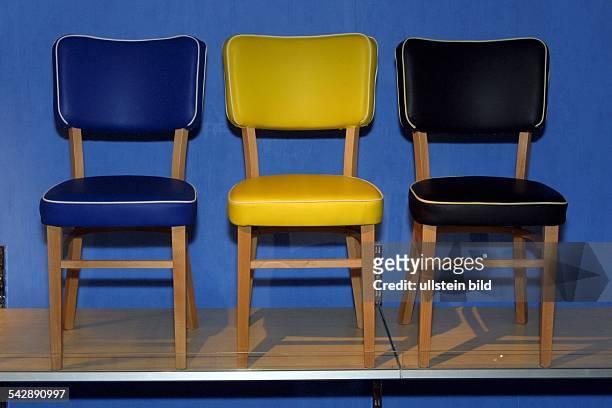 Drei gepolsterte Stühle im Möbelpark Sachsenwald. Jeder Stuhl ist in einer anderen Farbe gepolstert: blau, gelb, schwarz. Das Design ist amerikanisch...