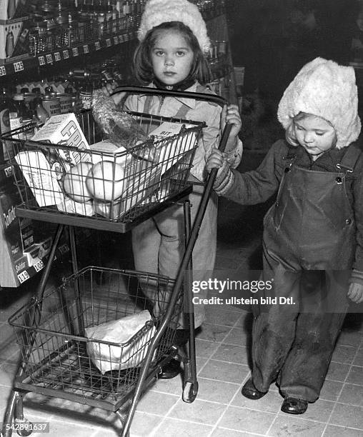 Einzelhandel Schweden: zwei kleine Mädchen mit Mützen schieben in einem Supermarkt einen Einkaufswagen an den Regalen vorbei.1949