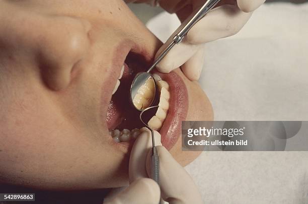 Zahnarztbesuch: Eine Patientin läßt ihre Zähne kontrollieren. Der Arzt prüft mit einem Mundspiegel und einer Sonde das gut gepflegte Gebiss der Frau...