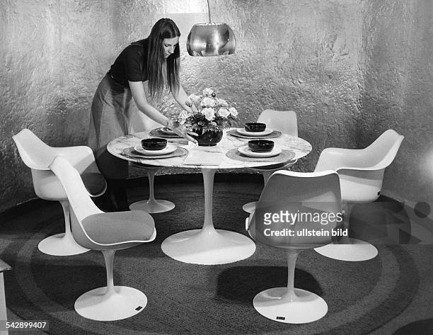 Esszimmer mit einem runden Tisch und Sitzmöbeln des finnischen Architekten Eero Saarinen : eine junge Frau arrangiert ein Blumengesteck auf dem...