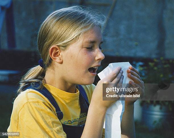 Ein Mädchen niest in ihr Taschentuch. Allergie; Niesen; Schnupfen. Symbolbild .