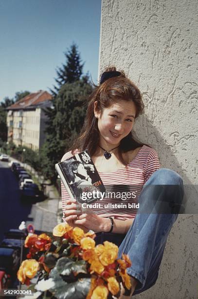 Die Schauspielerin Anna Lübbeke sitzt, ein Buch in den Händen, auf einer Balkonbrüstung mit Blumen. Undatiertes Foto.