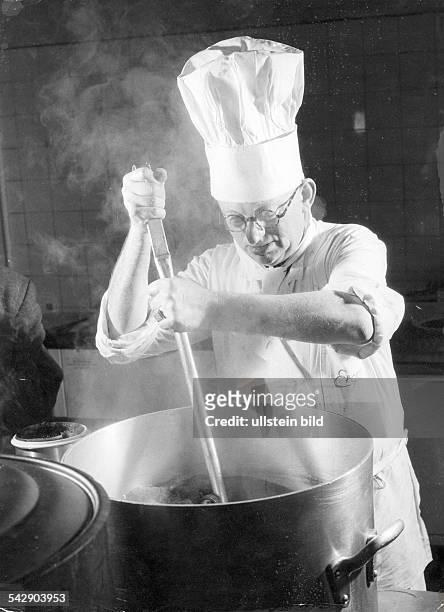 Ein Koch in einer Kantine rührt mit einem Kochlöffel in einem Topf1961