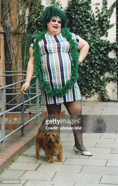 Der Travestie-Star Ulla Trulla steht in einem kurzen Minikleid, mit Pumps, einer grünen Federboa und einer Kopfbedeckung mit grünen Fransen auf einer...