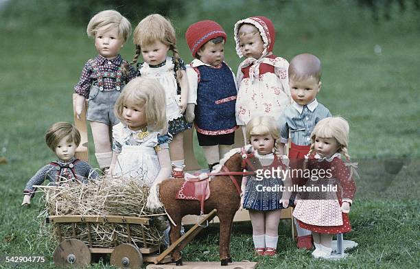 Eine Sammlung verschiedener Käthe-Kruse-Puppen ist auf einem Rasen zusammen mit einem Spielzeugpferd samt Heuwagen ausgestellt. Die Puppen stammen...