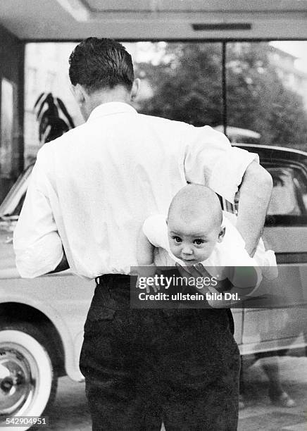 Ein Mann hat sich einen Säugling unter den Arm geklemmt1968