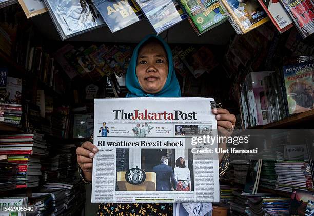 Vendor poses with the Indonesian newspaper The Jakarta Post which shows the cover headline which reads 'RI weathers Brexit shock', on June 25, 2016...