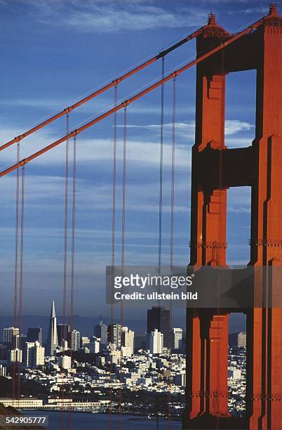 Blick durch die Stahlseile der Golden Gate Bridge auf San Francisco. Ein weißes Meer von Häusern und Wolkenkratzer hebt sich kontrastreich vom klar...