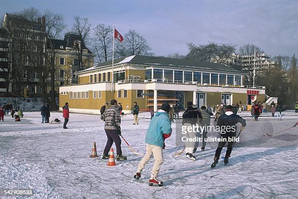 Eishockeyspieler auf der zugefrorenen Alster vor dem Germania-Ruderclub in Hamburg. Pylonen dienen als Feldbegrenzung. .