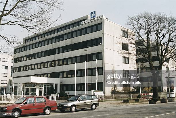 Kahle Bäume und zwei parkende Autos stehen vor dem Gebäude von "STN Atlas Elektronik". Am Dach befinden sich Schriftzug und Logo. Rechts eine...