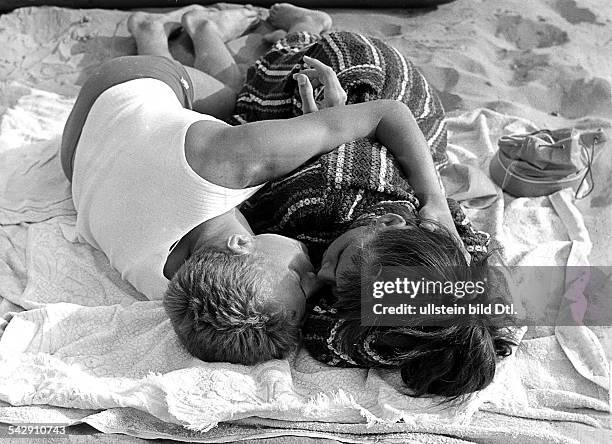 Ein junges Paar liegt auf einem Badehandtuch am Strand und küsst sich1958Foto: Gert Kreutschmann