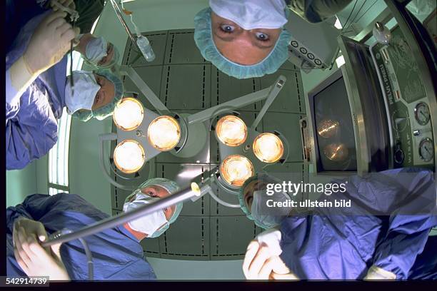 Operation: Anästhesieärzte und Chirurgen beugen sich über einen Patienten. Darüber die schwenkbare Operationslampe. Ärzteteam; Anästhesist; Chirurg;...