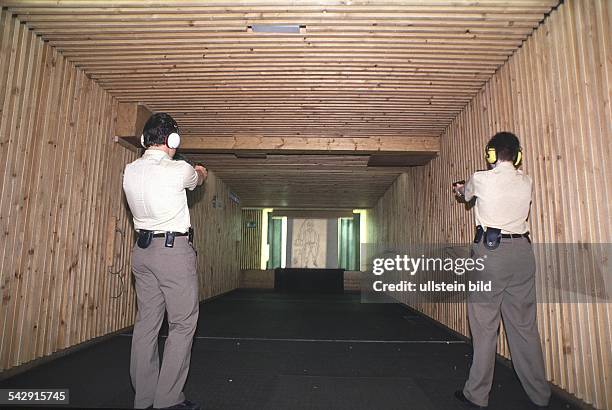 Zwei Polizisten während einer Schießübung. Mit beiden Händen halten die Beamten ihre Dienstpistole und zielen auf die Zielscheibe. Zum Schutz gegen...