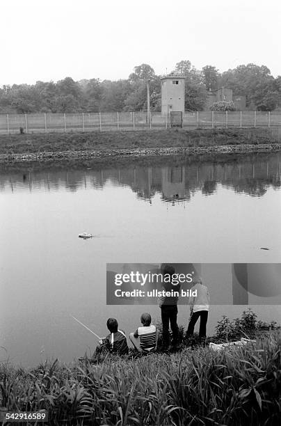 Kinder spielen mit einem ferngesteuerten am Teltowkanal, im Hintergrund ein Wachturm an den Grenzanlagen der DDR- April 1984