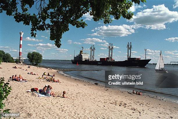 Hamburg: ein Sommertag am Strand von Blankenese. Einige Sonnenhungrige liegen im Sand. Auf der Elbe fahren ein Containerschiff und ein kleines...