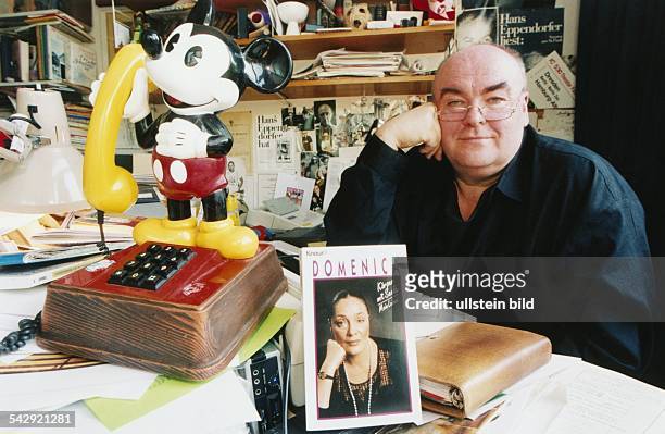 Schriftsteller Hans Eppendorfer am Schreibtisch mit seinem Buch über Domenica Niehoff. Links befindet sich ein Mickey-Mouse-Telefon. .