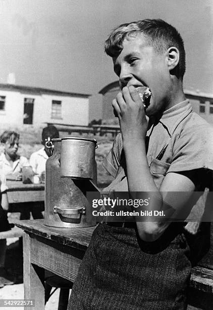 Ein Junge mit einem Brötchen und einem Becher Milch in der Pause - 1935