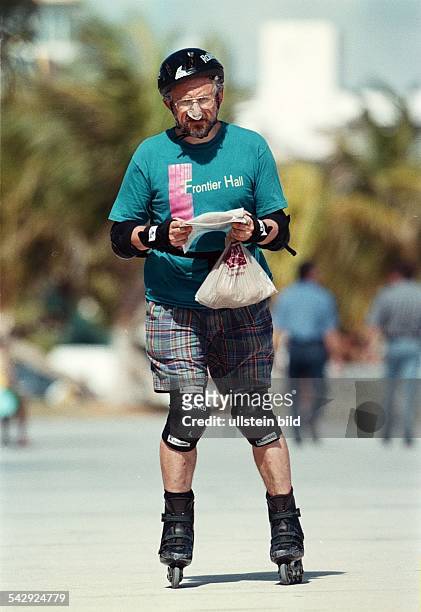 Älterer Mann / Senior beim Inline-Skaten auf der Strandpromenade von Miami. Er trägt Helm, Nasenpflaster als Sonnenschutz, Ellbogen- , Hand- und...