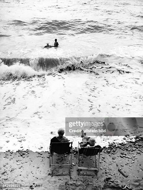 Zwei ältere Menschen sitzen auf Liegestühlen direkt am Meer1969