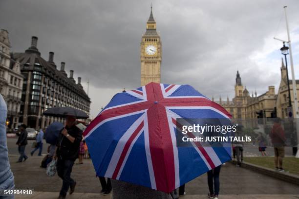 Pedestrian shelters from the rain beneath a Union flag themed umbrella as they walk near the Big Ben clock face and the Elizabeth Tower at the Houses...
